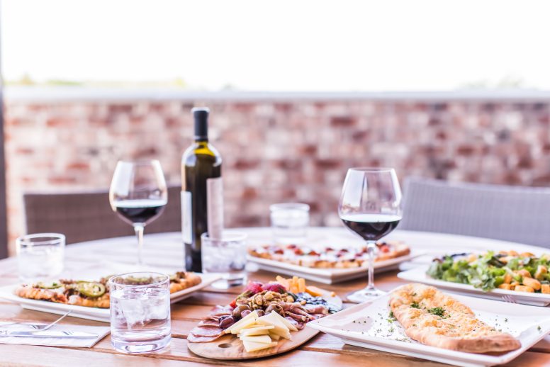 A patio table with a variety of flatbread pizzas, and a bottle of red wine.