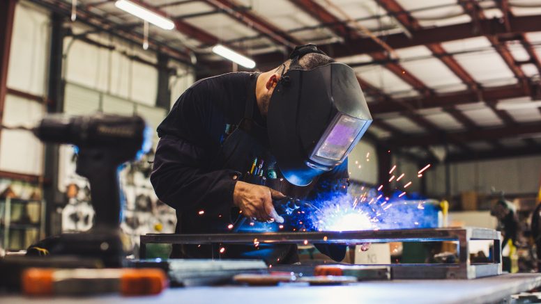 A welder wearing protective gear  is torching metal.