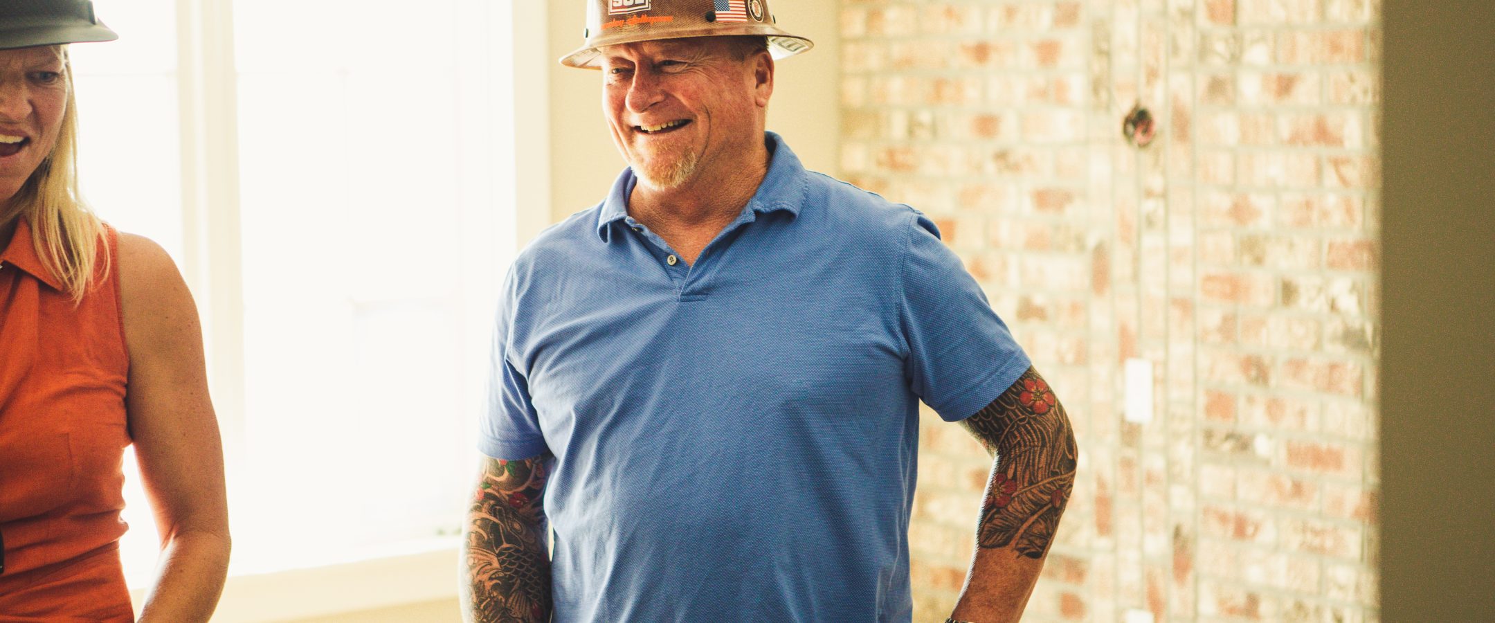 Older man in blue shirt with hands on hips standing by a window