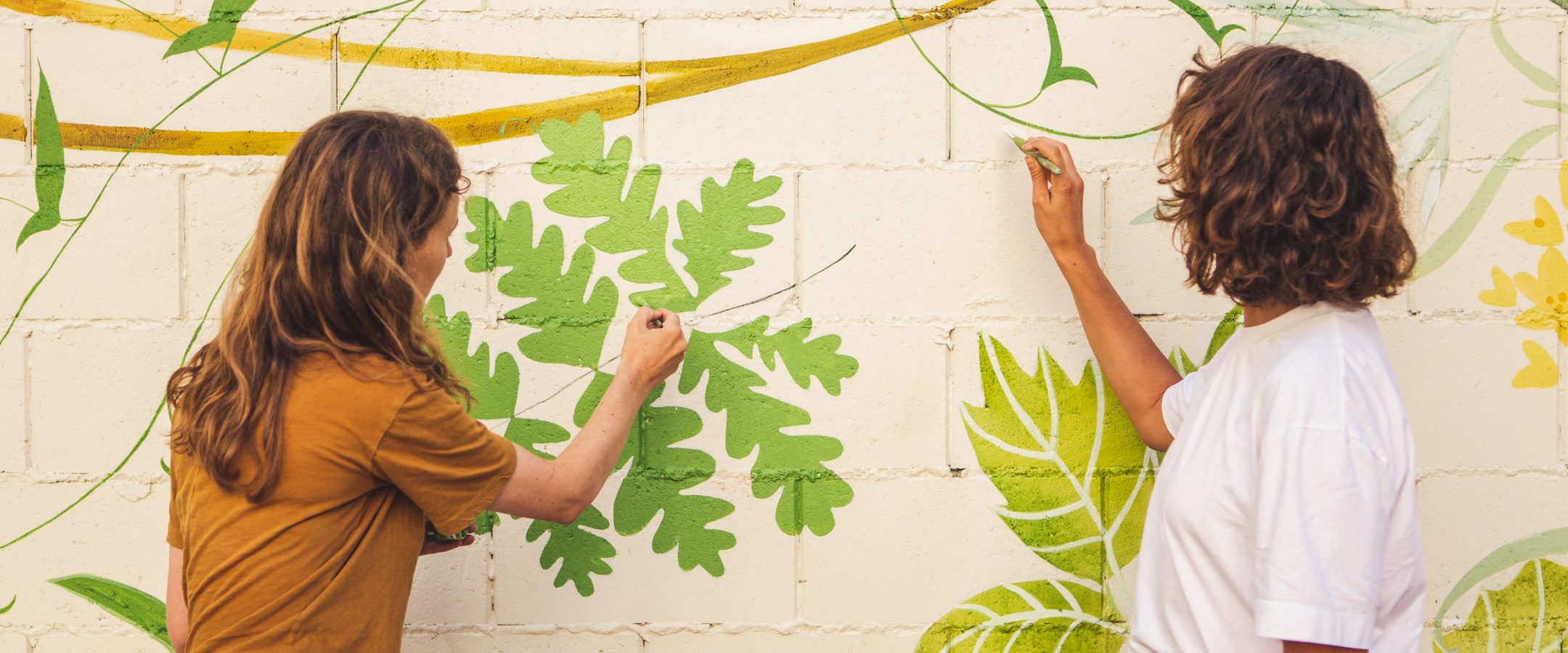 Two women painting a floral mural