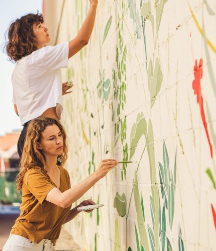 Two woman painting a floral mural on a wall