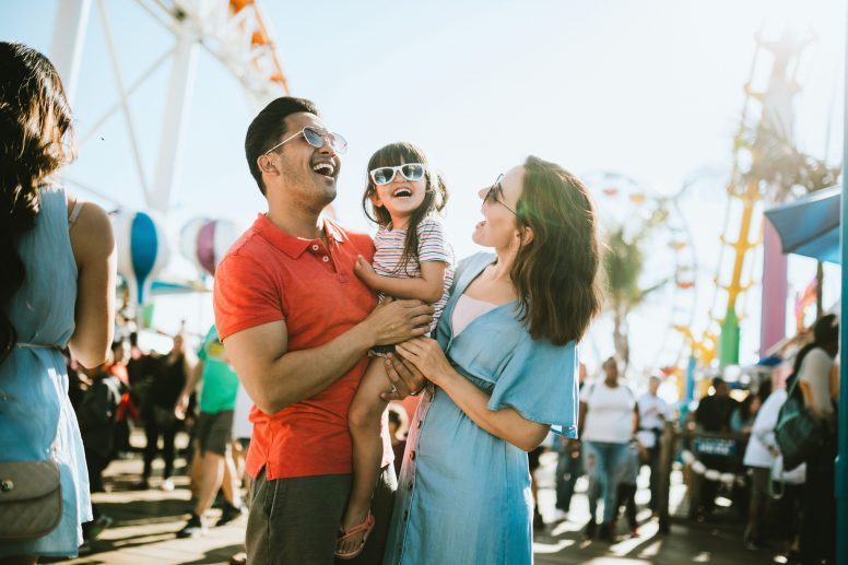 A cute mixed race family enjoys the rides and sun at the fair activities. They all wear sunglasses with big smiles.