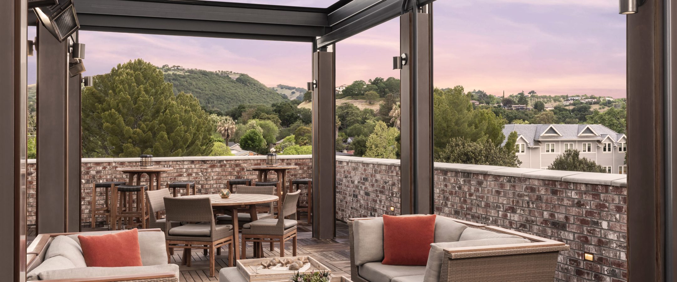 A roof top patio with comfortable seating, fire pits and a view of the sunset on the horizon.