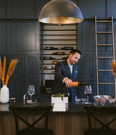 A sommelier pouring win at a wine bar. There is wine refrigerator behind him.