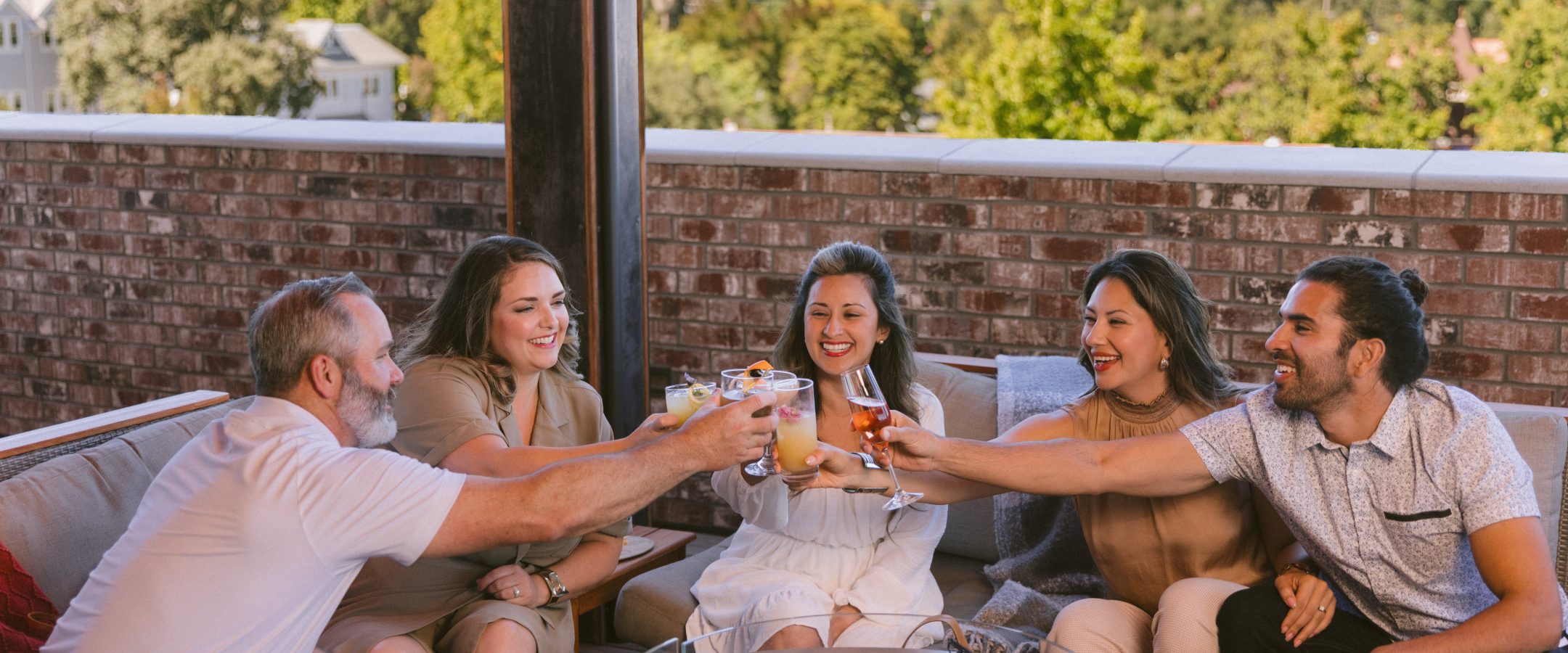 A group of friends around a fire pit on a rooftop bar toasting with cocktails.