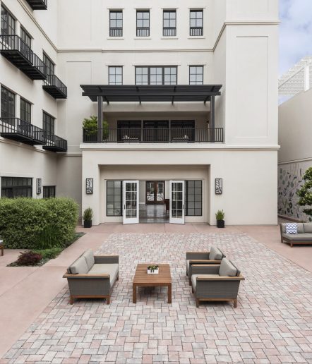 A modern outdoor courtyard with brick flooring, featuring seating arranged around a central table.