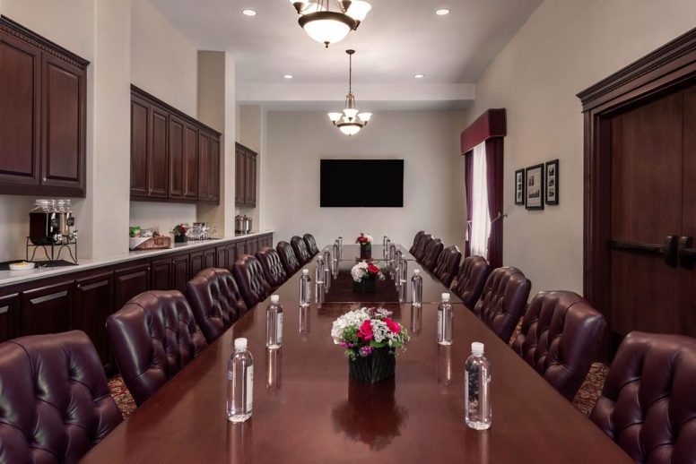 A conference rooms with red chairs and red oak table with water bottles in front of each seat.
