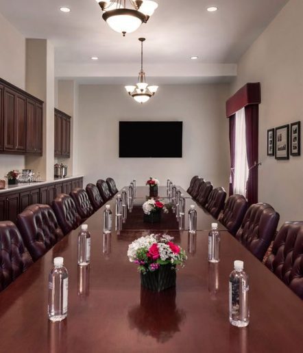 A meeting room with a large long wooden table and several executive padded chairs on the left and right sides of the table with bottles of water placed in front of each seat.