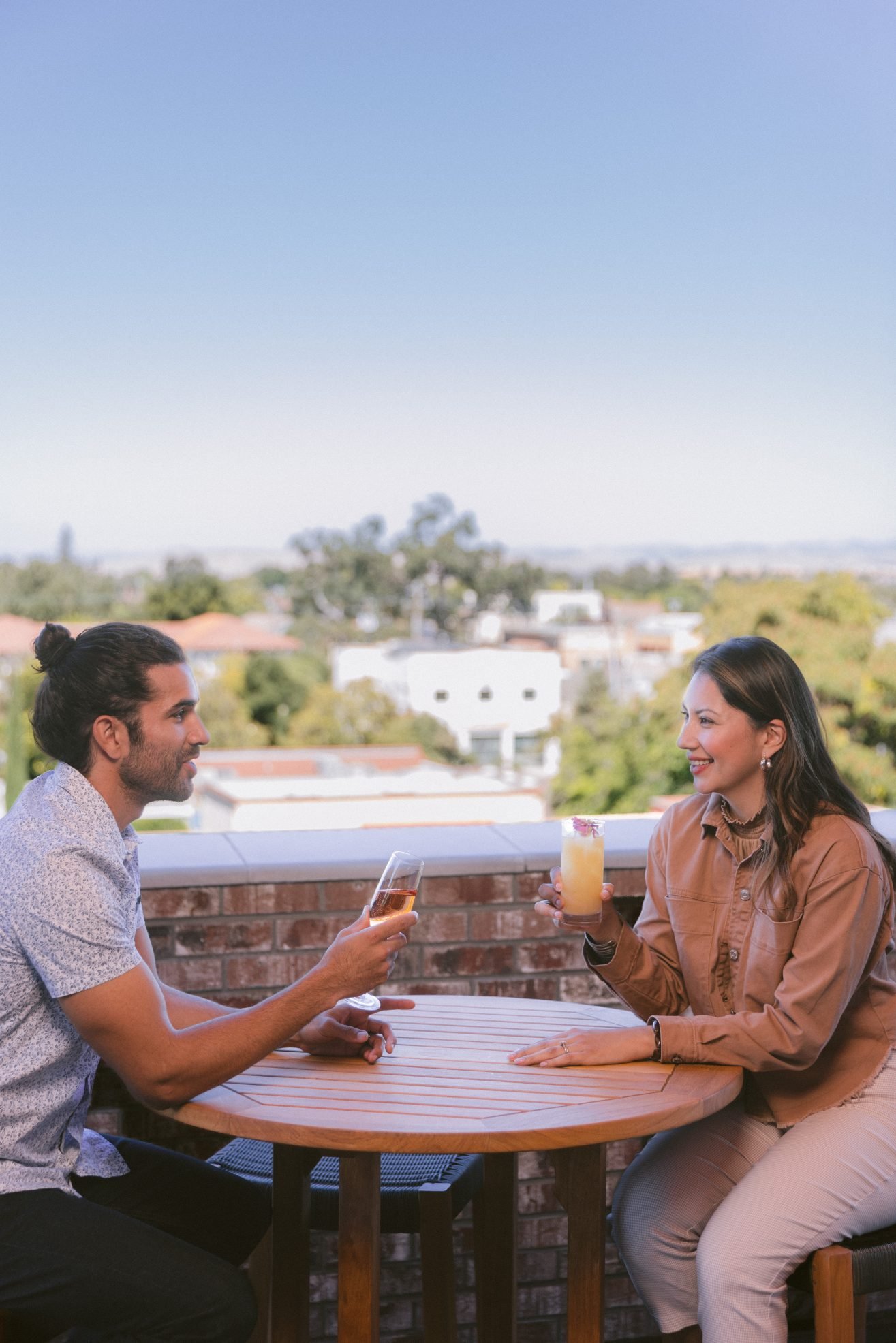 A man and a woman on a rooftop sitting at a table having drinks