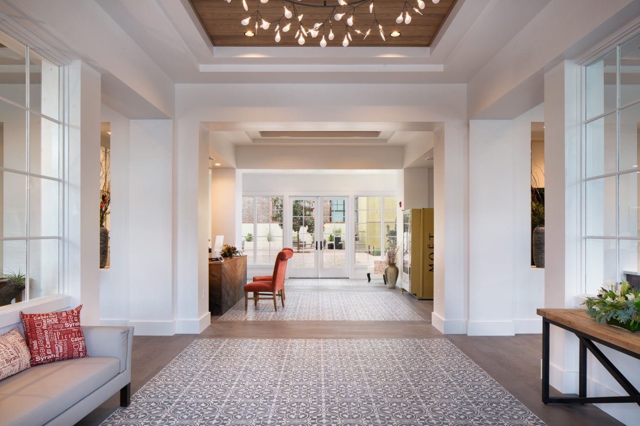 hotel lobby with reception desk, two orange chairs, a champagne vending machine, a sofa, side table and fancy patterned floors