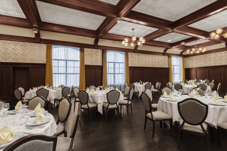 Banquet room with round tables that seat six and is set with white tablecloths, yellow napkins and place setting.