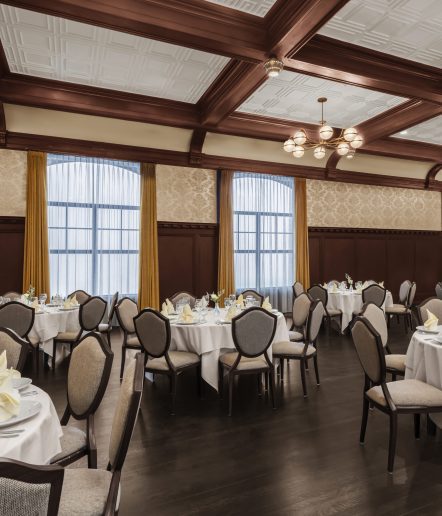 Banquet room with round tables that seat six and is set with white tablecloths, yellow napkins and place setting.