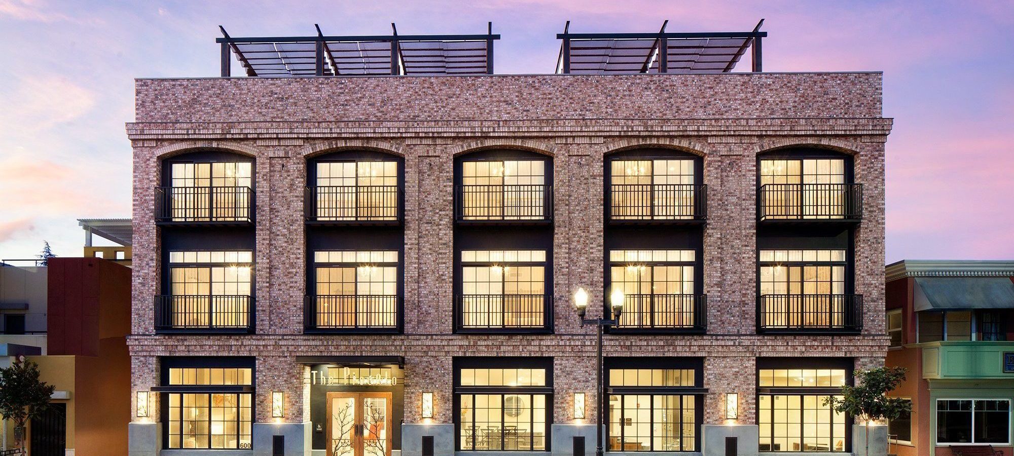 Exterior of a brick building with 6 windows seen at night with the interior lights shining.