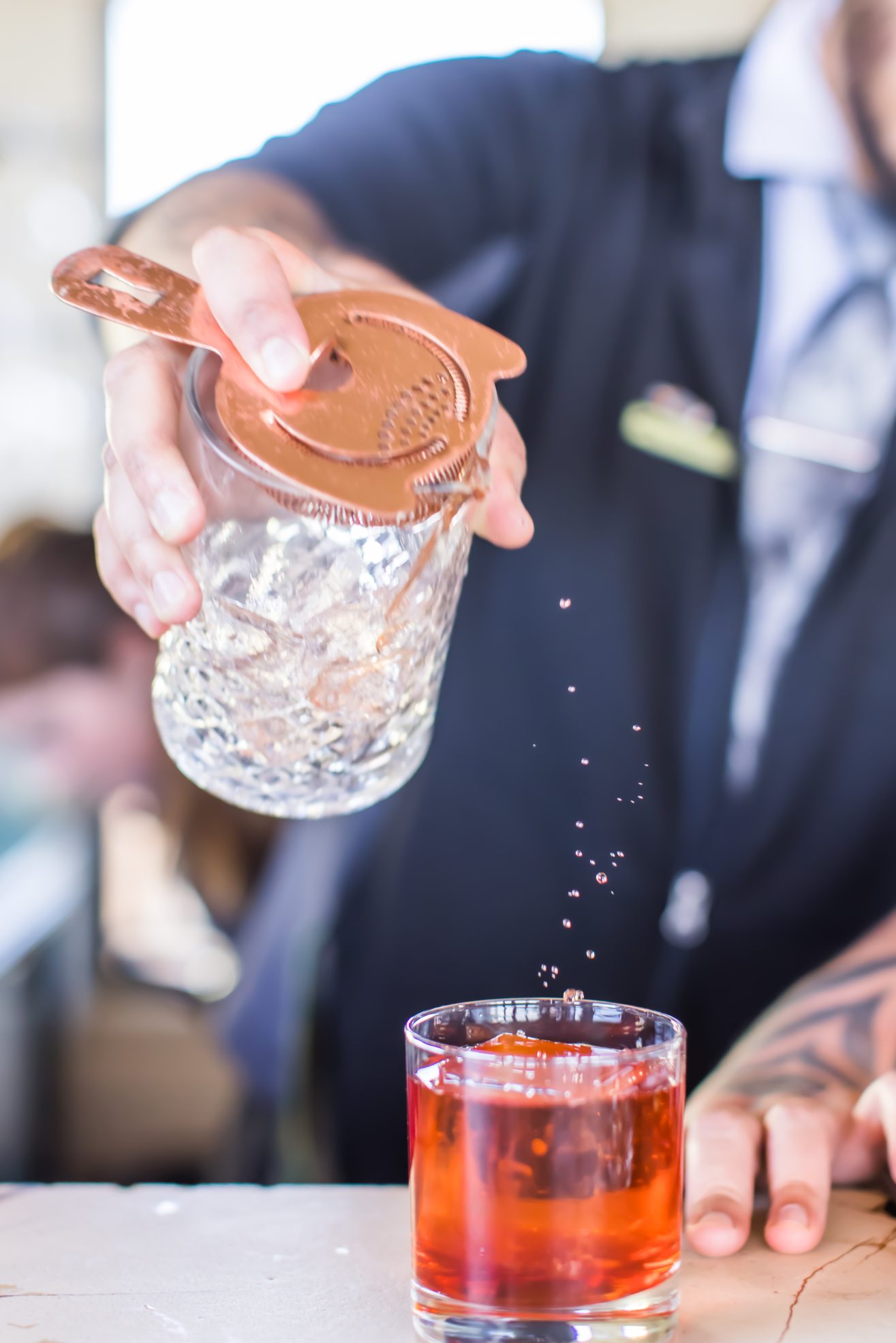 A close up of a bartender's torso as they pour a drink from a crystal cylinder into a glass.