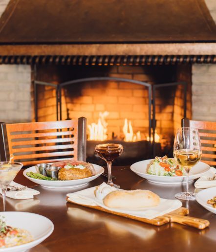 Close up of dinner dishes on a table with a roaring fire behind.