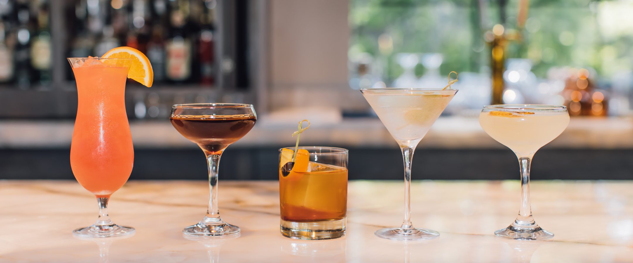 Cocktails in different glasses on a bar.