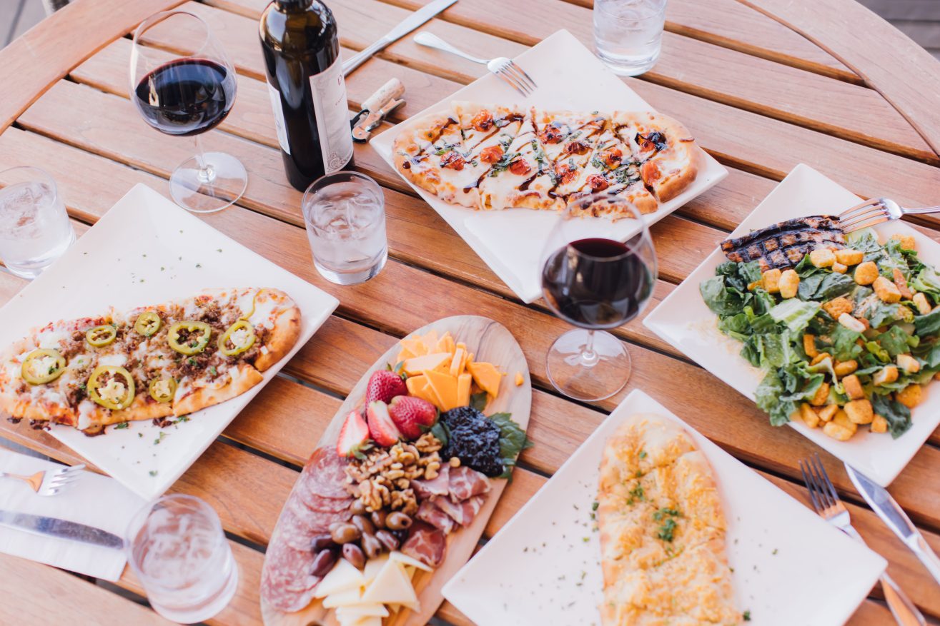 A picnic table with a variety of flatbread pizzas and a bottle of win