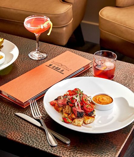 Close up of a table with plates of food, a menu and a cocktail on top.