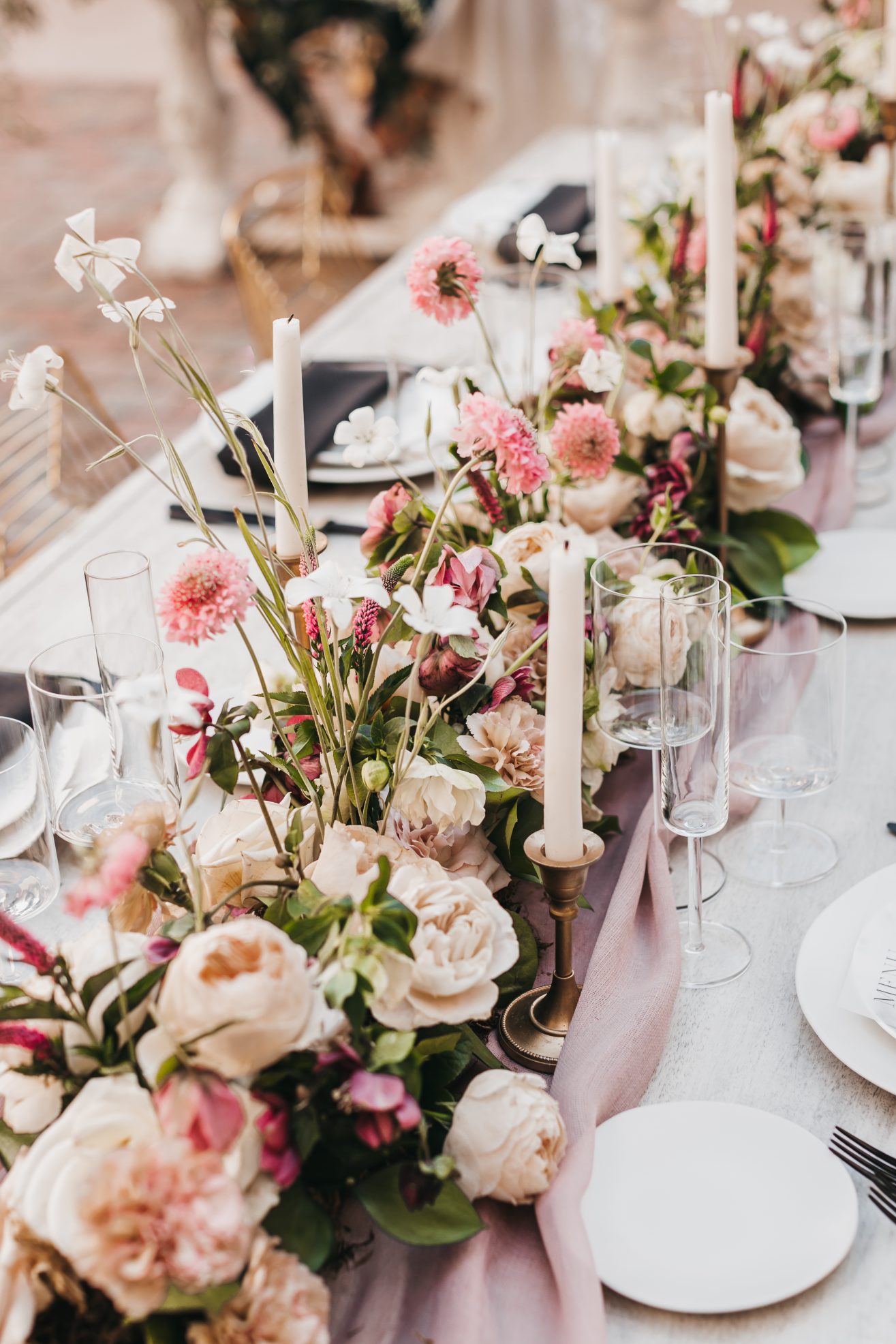 A table arrangement of dishware, silverware, candle sticks, pink and white florals.