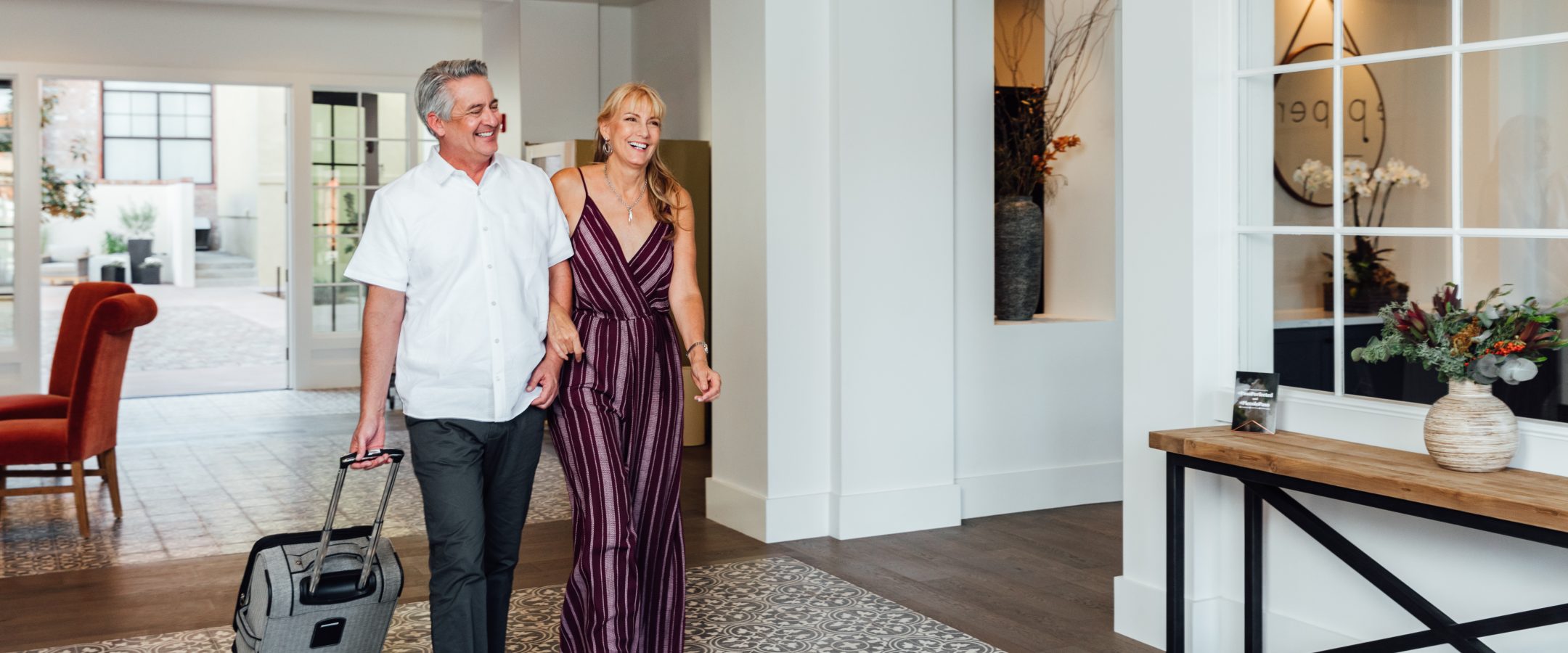 A man and woman holding hands pulling a suitcase as they enter a hotel lobby