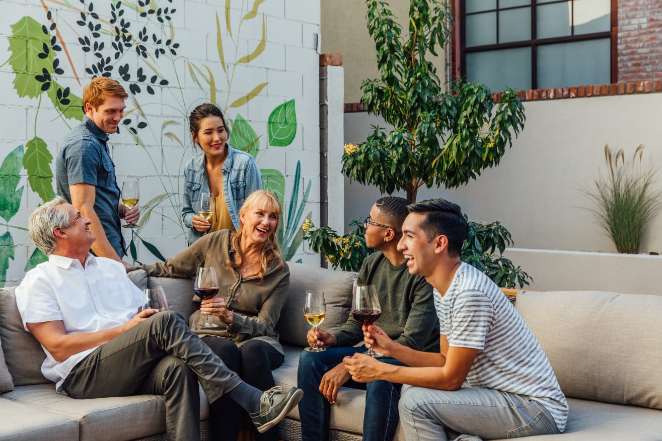 A group of friends relaxing together, some seated and some standing, holding wine glasses.