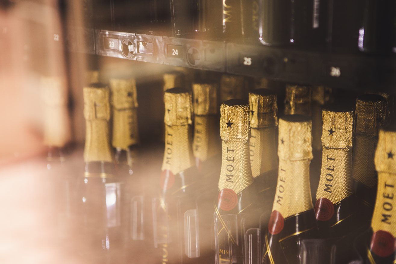 Close up shot of several mini moet champagne bottles lined up inside a vending machine.