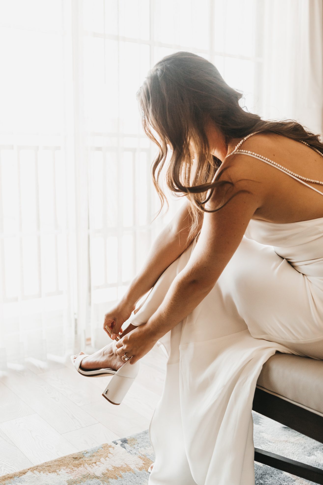 A woman in a white dress putting on her heeled shoes.