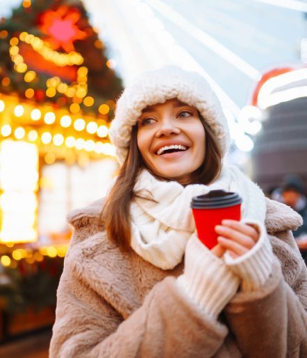 Happy woman with disposable paper coffee cup in winter over outdoor ice skating rink on background. Christmas, hot drinks and holidays concept.