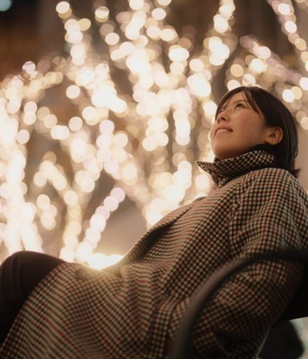 A portrait of an Asian woman sitting under Christmas illumination lights in the city at night.