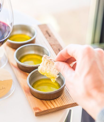 Olive oil tasting - 3 oils are in small bowls. A hand dips bread into one bowl.