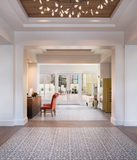 hotel lobby with reception desk, two orange chairs, a champagne vending machine, a sofa, side table and fancy patterned floors