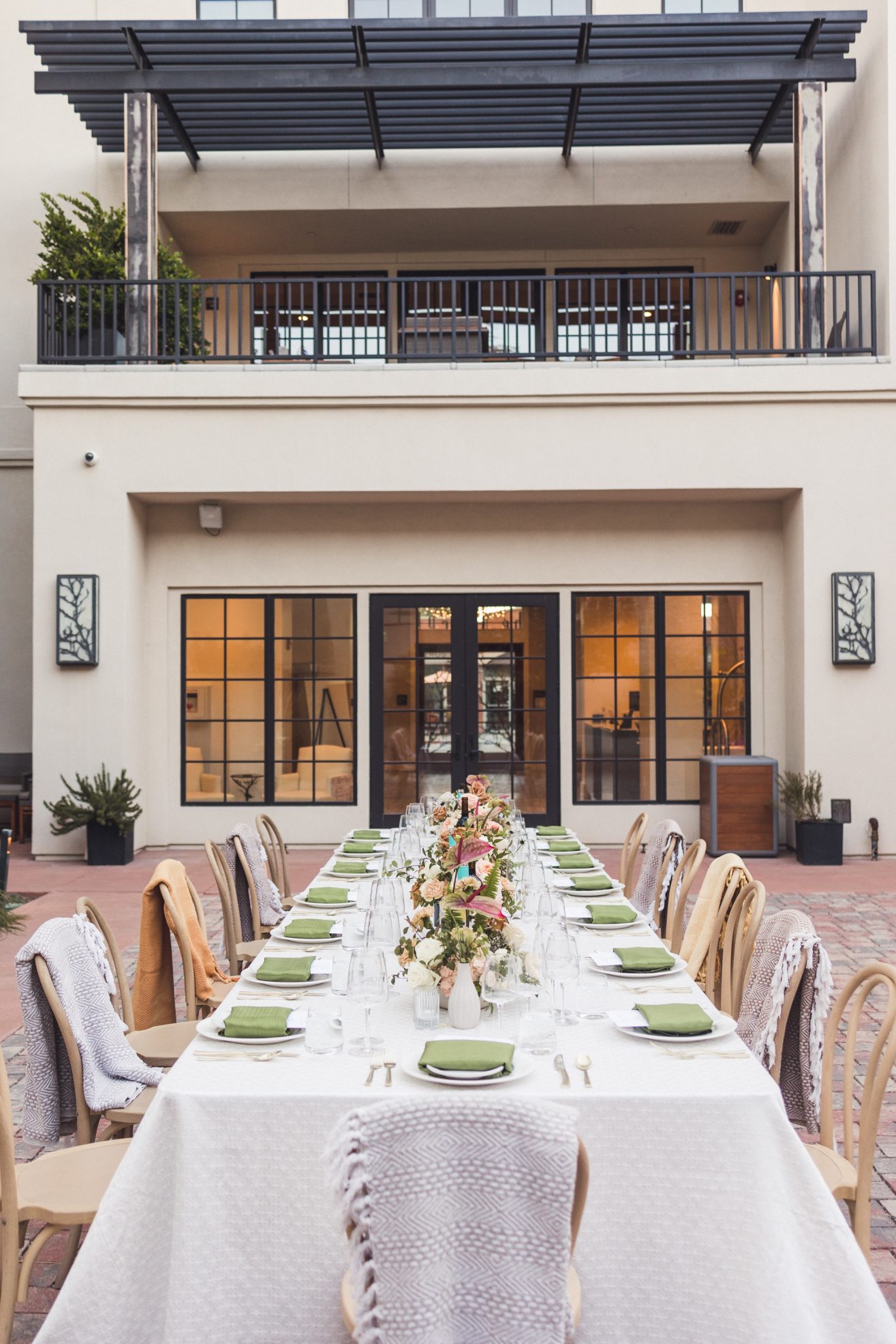 Table set with white linens, green cloth napkins, menus on top of plate, and color floral arrangements.