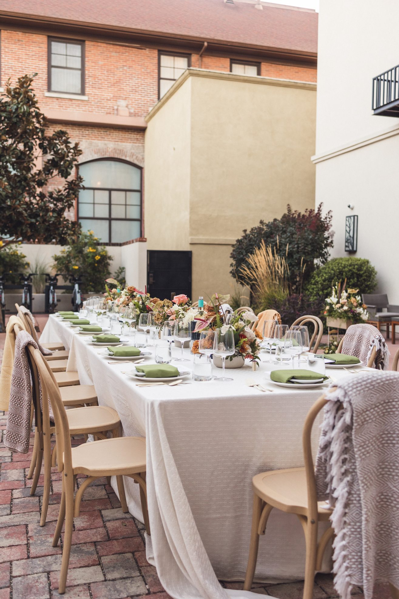 Table set with white linens, green cloth napkins, menus on top of plate, and color floral arrangements.