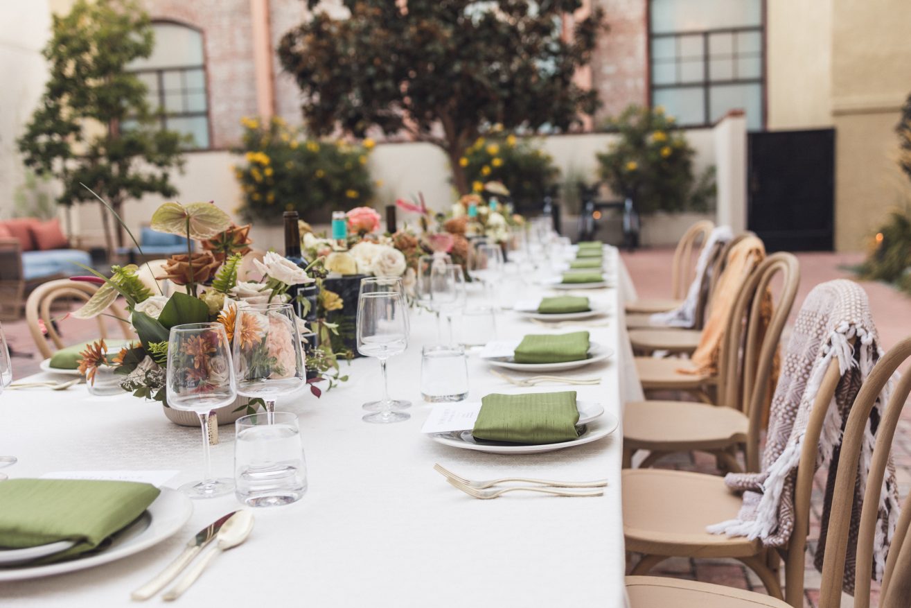 Table set with white linens, green cloth napkins, menus on top of plate, and color floral arrangements.