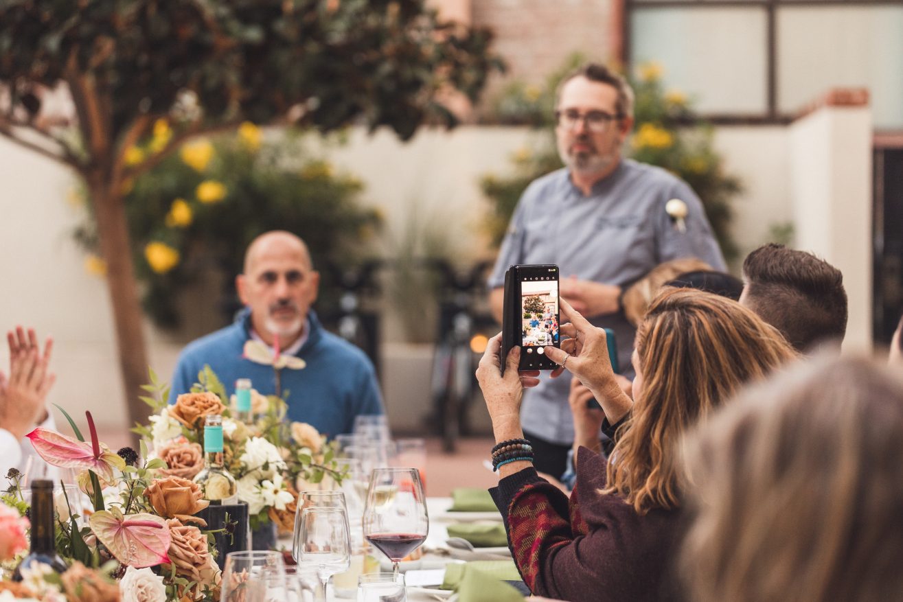 Man in blue shirt next to chef in chef coat at a dinner party in a courtyard.