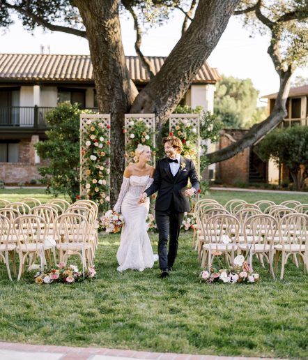 Bride and Groom walking down grass aisle with oak tree in background