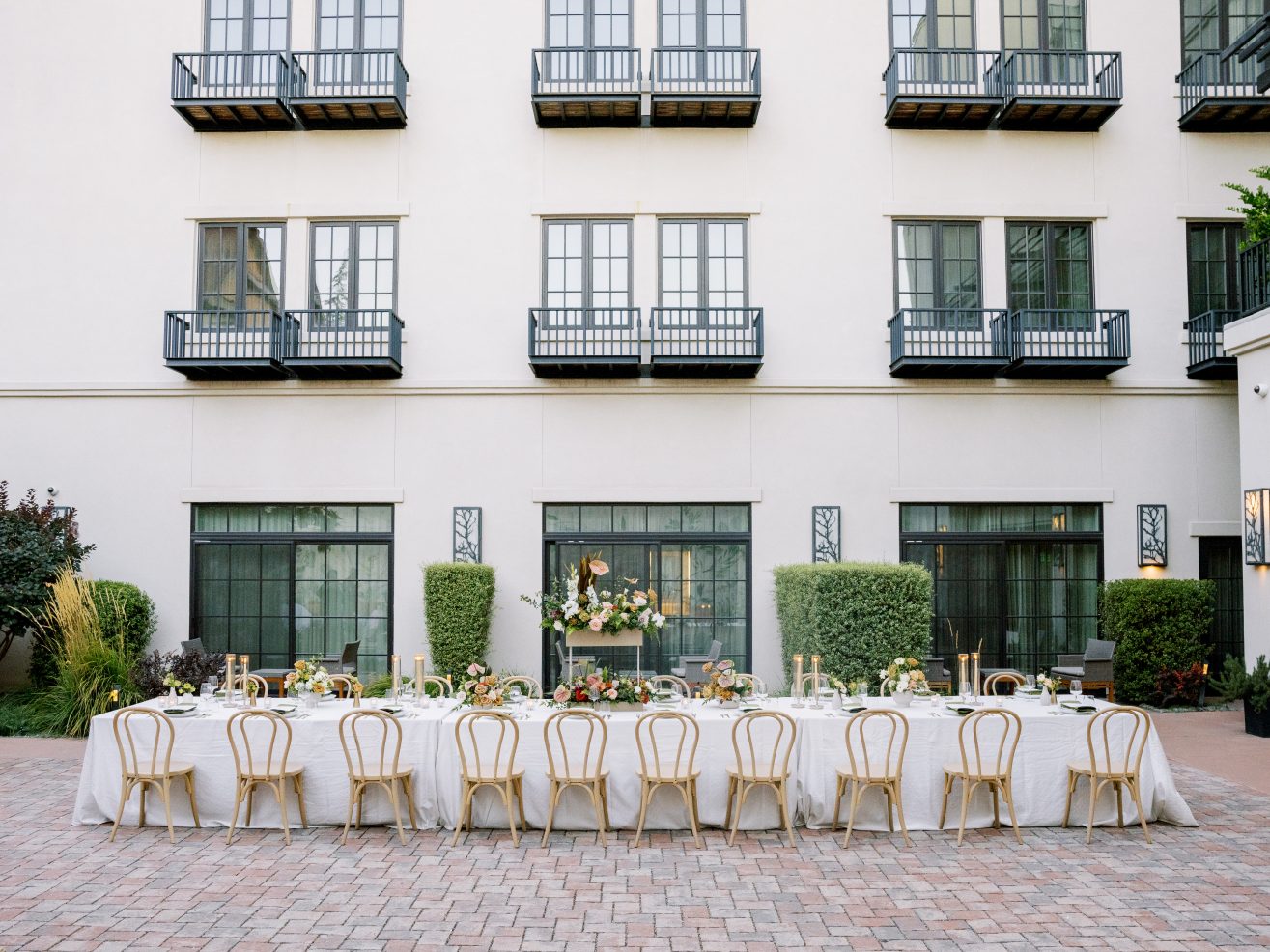 Long table in courtyard set with wooden chair for a private dinner.