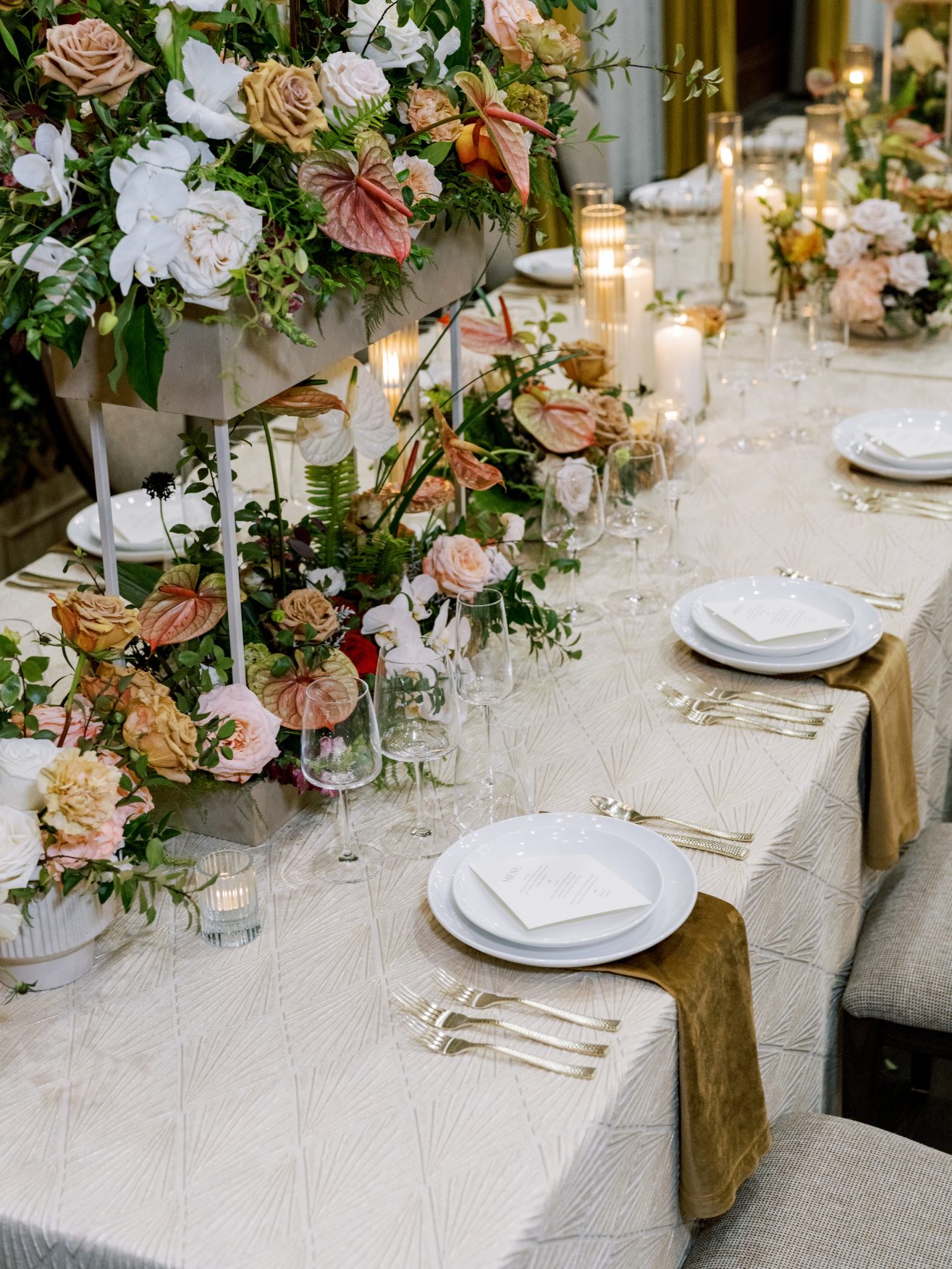 A table set with candles and several bouquets of colorful flowers.