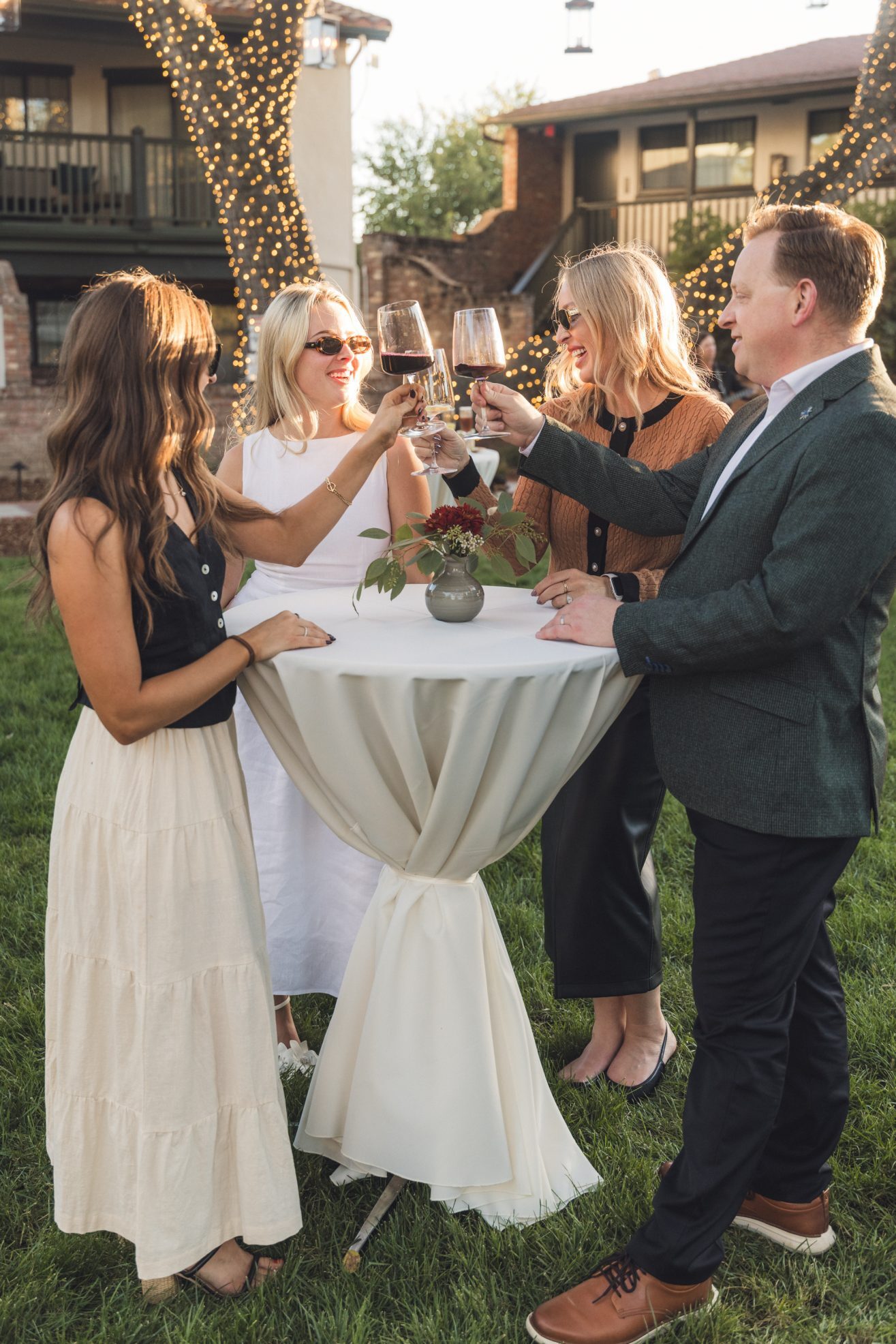 Three women and 1 man enjoying wine in a lighted garden of oak trees.